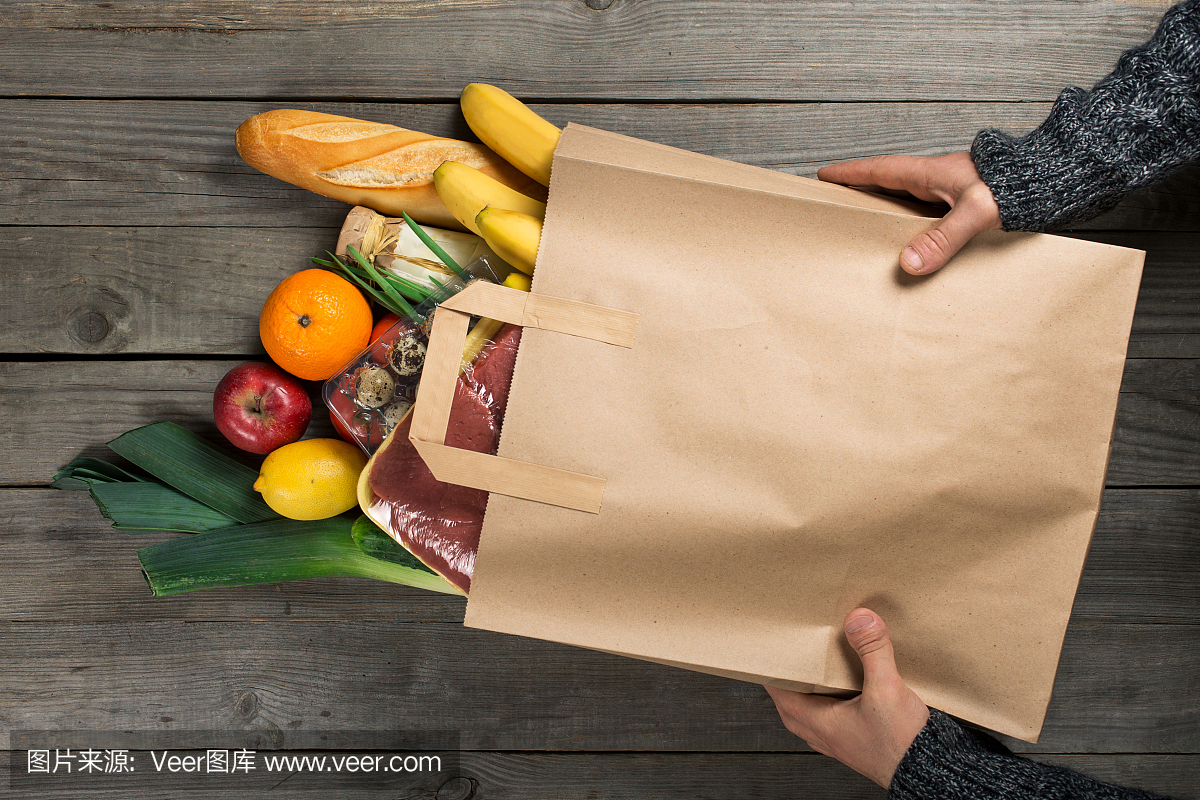 男人拿着袋子不同的健康食品在木制厨房